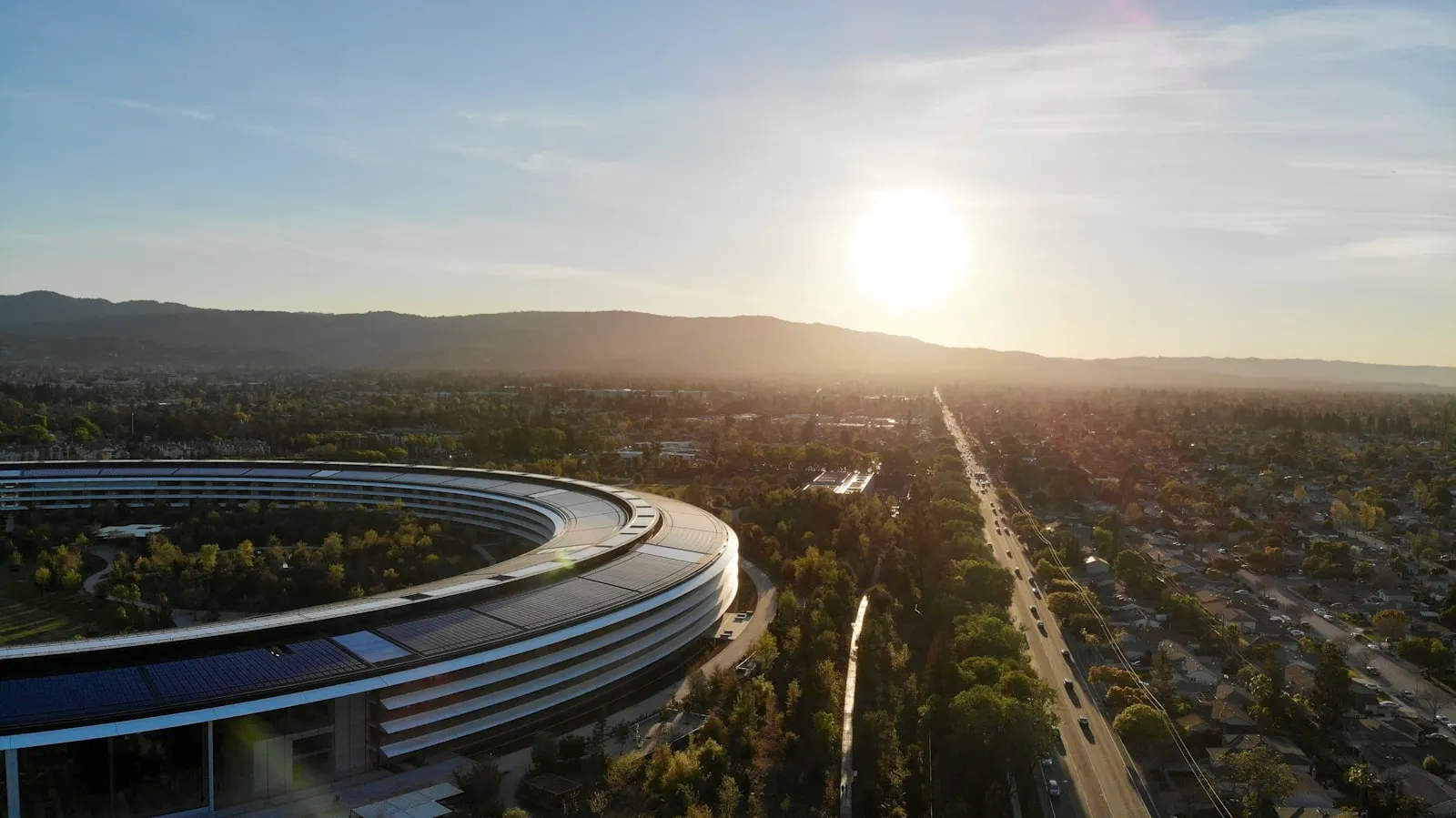 日落时分 Apple Park 环形主楼的航拍，远处是山脉与住宅区
