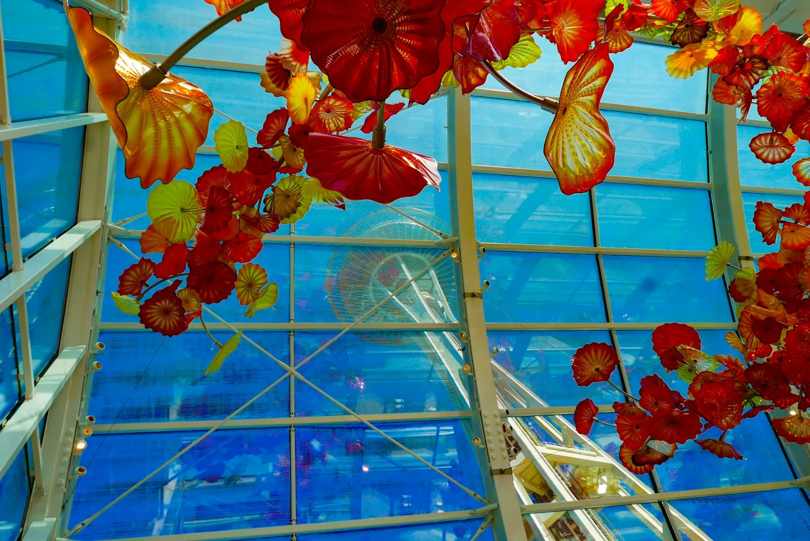 Chihuly Glasshouse 玻璃屋顶下悬挂的红橙色玻璃花朵雕塑，透过玻璃能看到太空针
