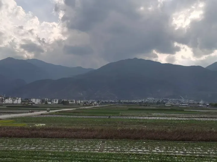 大理海西沿途田园风光，整齐的农田一直铺到山脚，远处是连绵青山与厚重云层