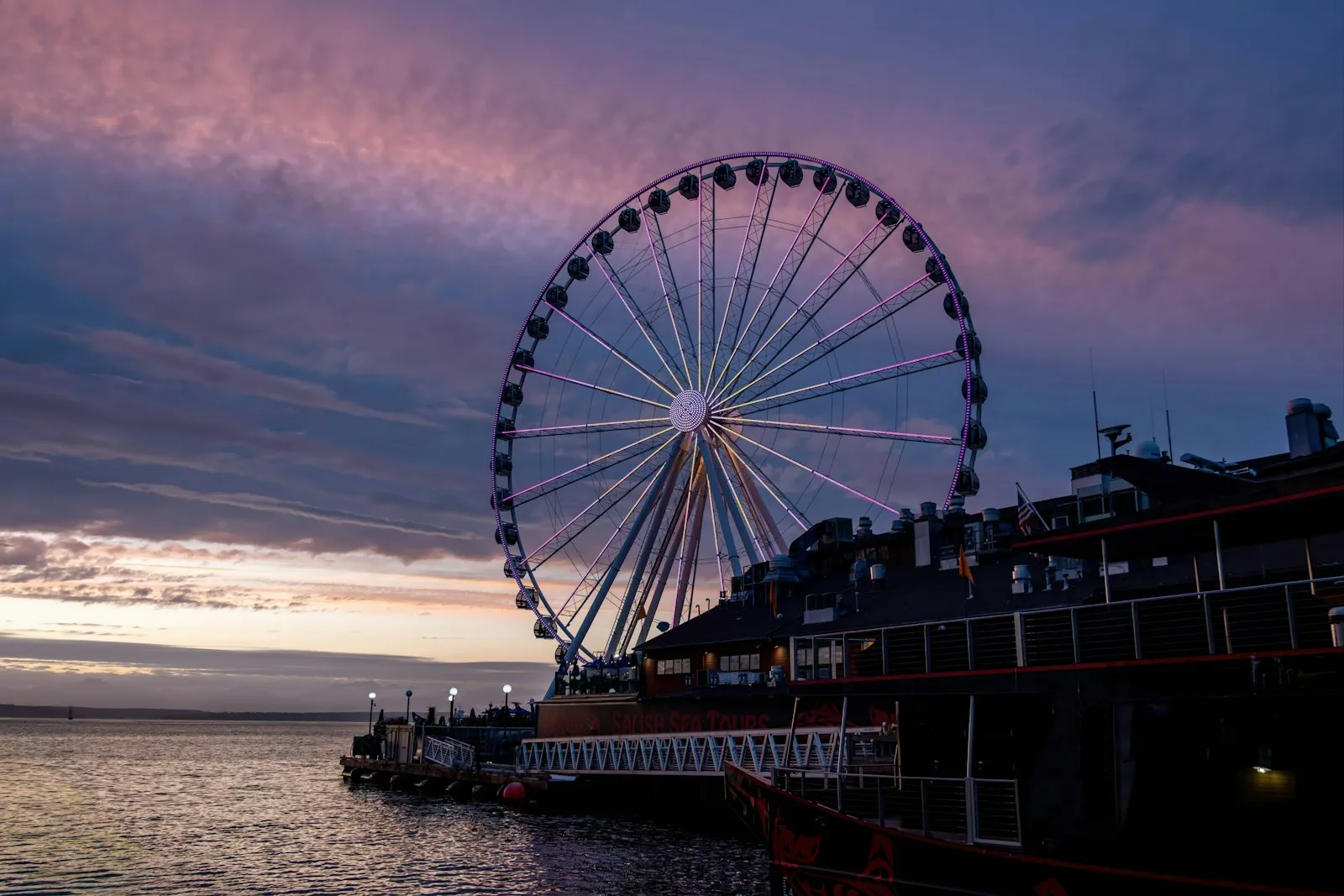 蓝调时刻亮起紫色灯光的 Seattle Great Wheel，倒映在 Elliott Bay 的水面上
