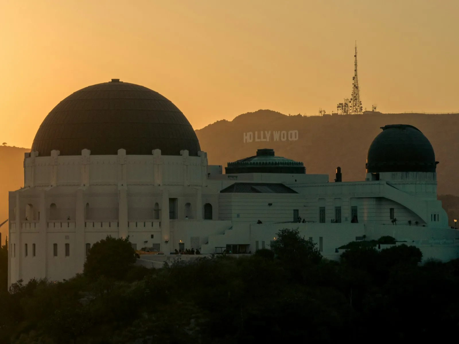 日落时 Griffith Observatory 的圆顶剪影,远处山坡上是 Hollywood 字牌