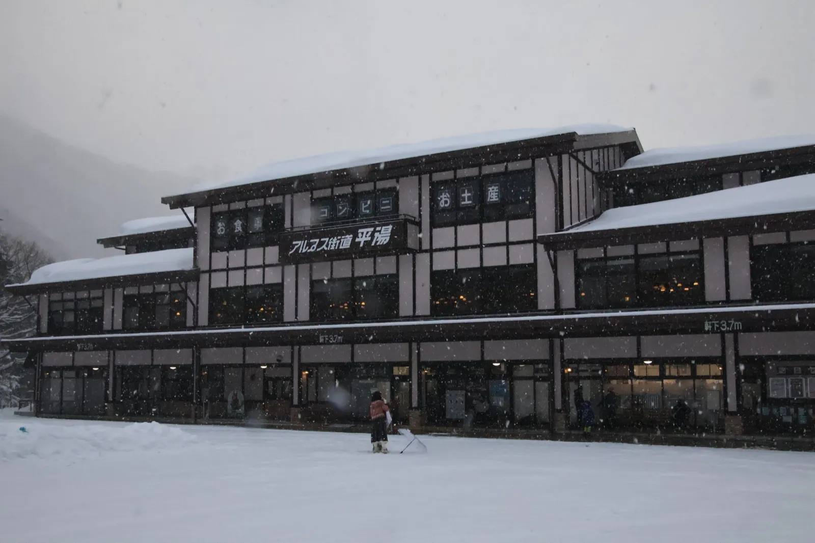 大雪中的平汤温泉街,一栋写着「アルプス街道 平湯」的传统建筑屋顶覆满积雪