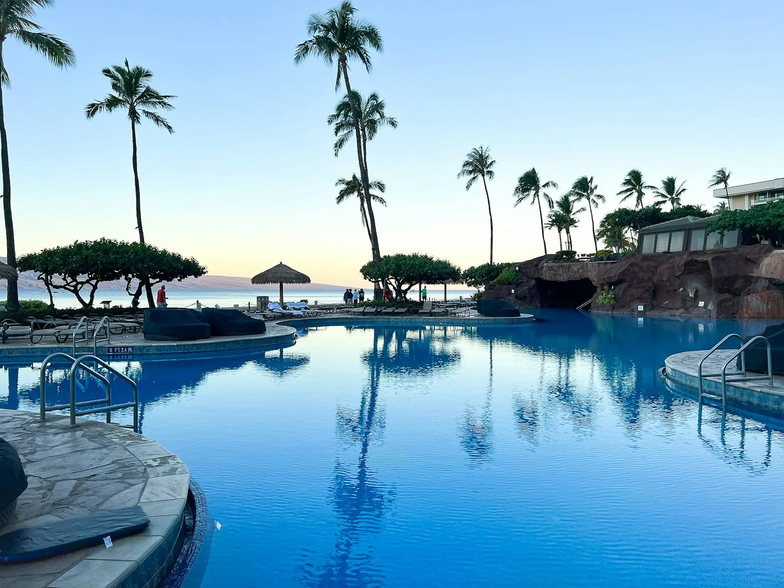 清晨蓝调时刻 Hyatt Regency Maui 的泳池，棕榈树倒映在水面，远处是 Lānaʻi 岛