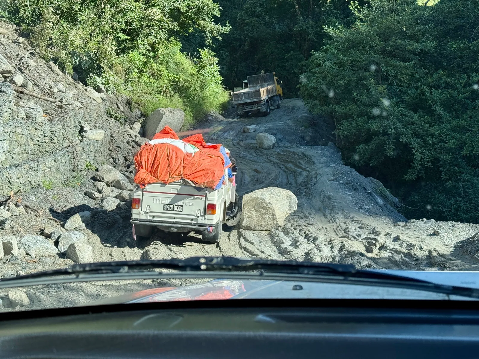 一辆吉普车行驶在塌方碎石遍布的土路上，前方还有一辆卡车
