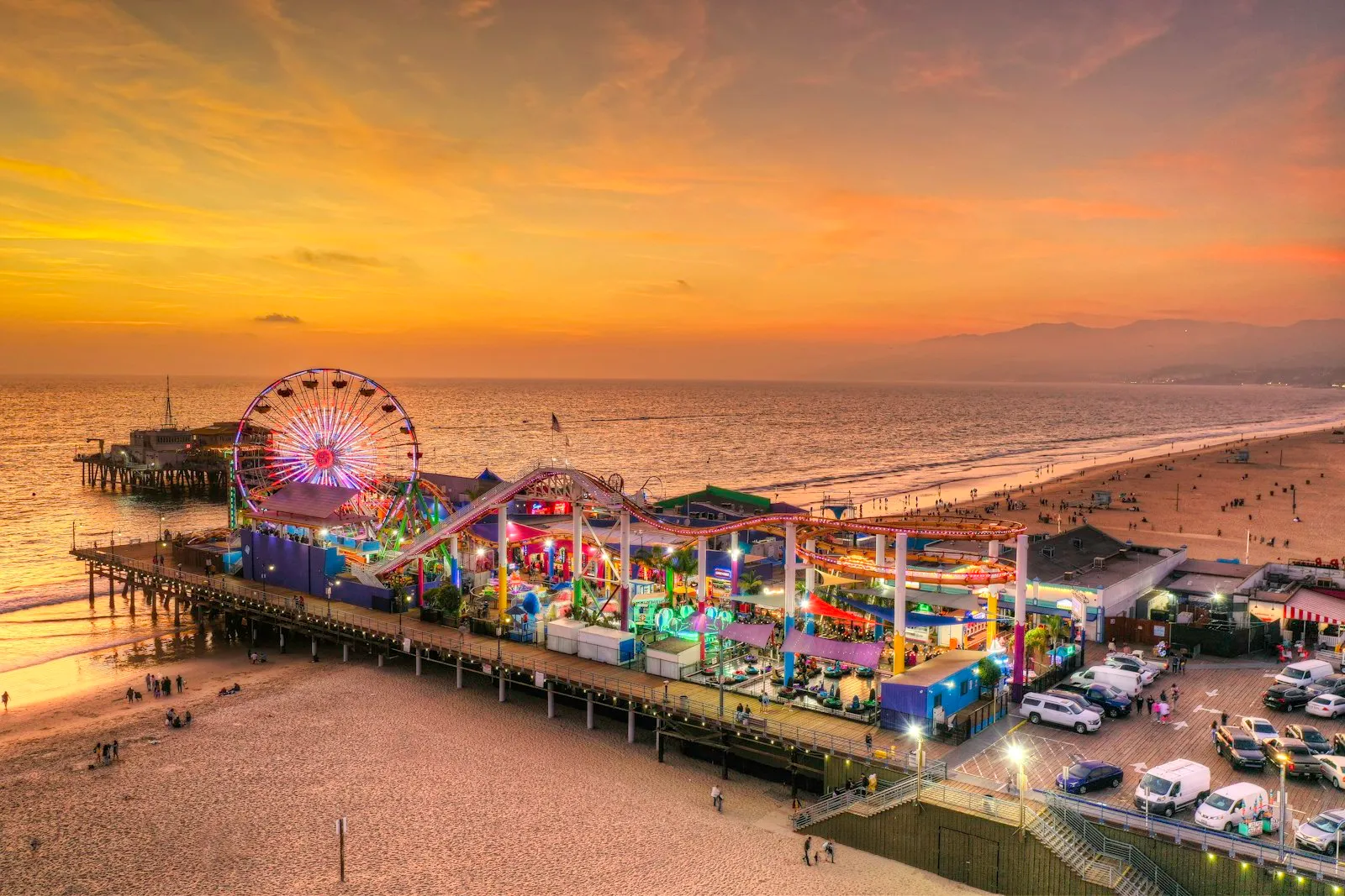 黄金时刻航拍 Santa Monica Pier,摩天轮亮着灯,沙滩、海面与远处的山脉都染成金色