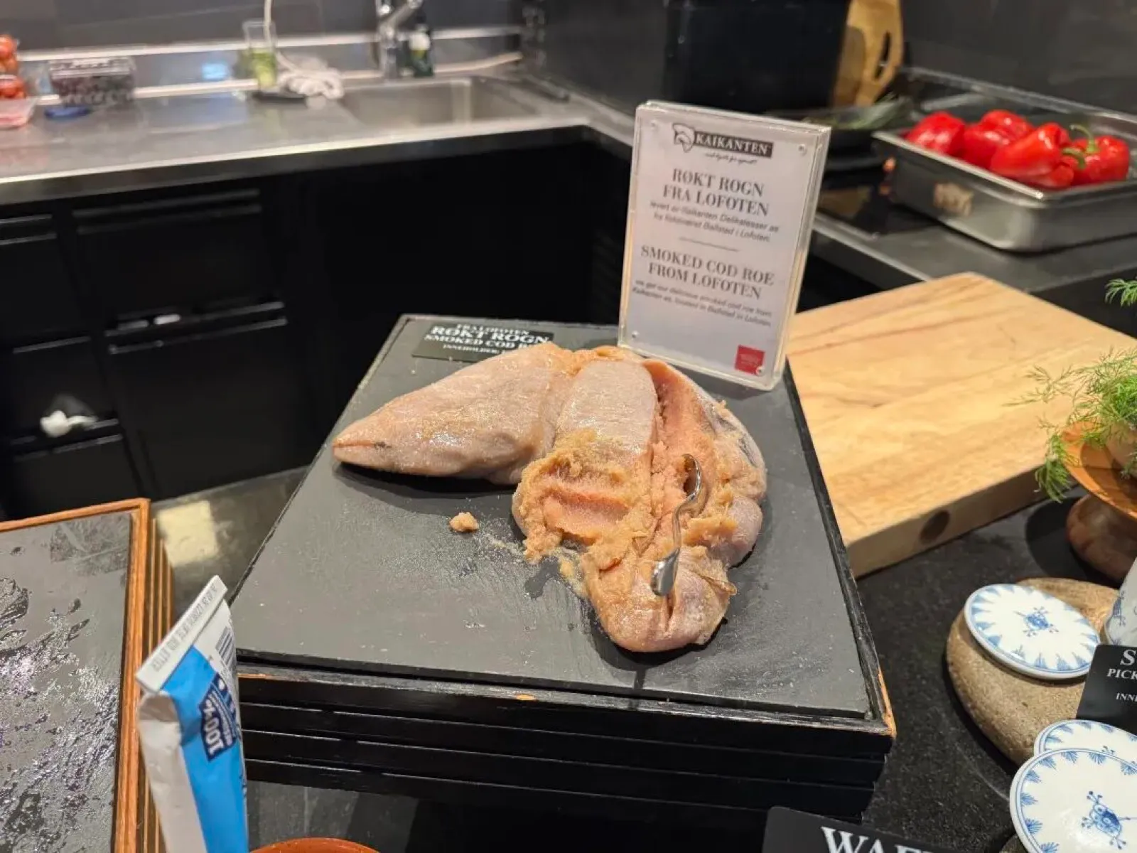 黑色石板上摆着来自罗弗敦的烟熏鳕鱼籽,配有英文标签 SMOKED COD ROE FROM LOFOTEN,旁边是樱桃番茄与切菜木板