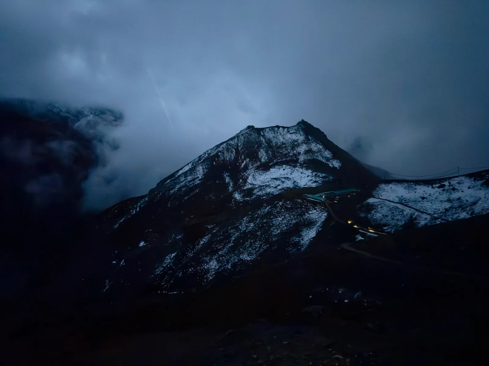 黎明前幽蓝的天色下，覆雪的山脊轮廓与山间几点高营地灯火