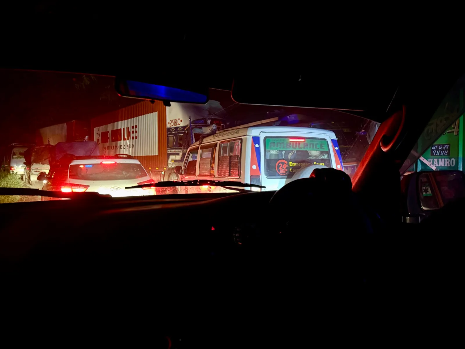 夜晚透过车窗看到前方堵着的救护车与车流，红蓝灯光在黑暗中格外醒目