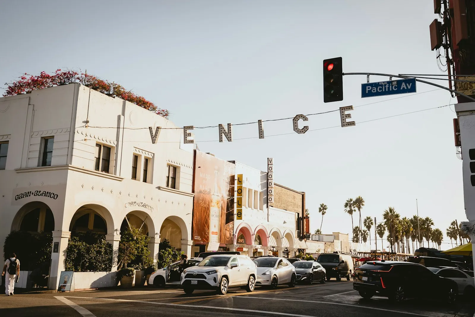 横跨 Windward Ave 的 VENICE 灯泡字招牌,下方是白色拱廊建筑和棕榈树