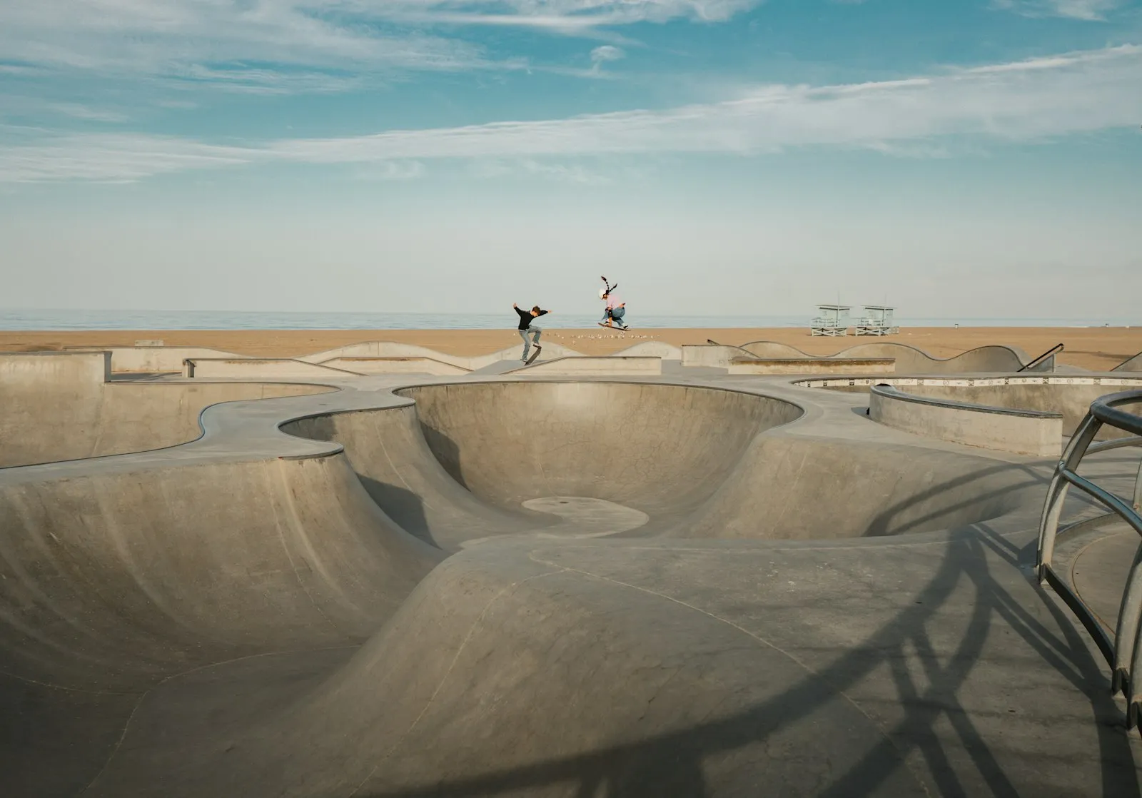Venice Beach 的滑板碗池,两名滑手在空中,背景是沙滩和救生员塔