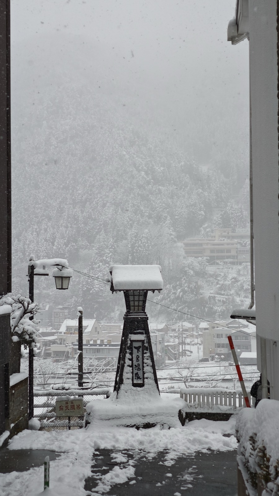 大雪中的下吕温泉街，石灯笼积着厚雪，山坡下是层叠的温泉旅馆