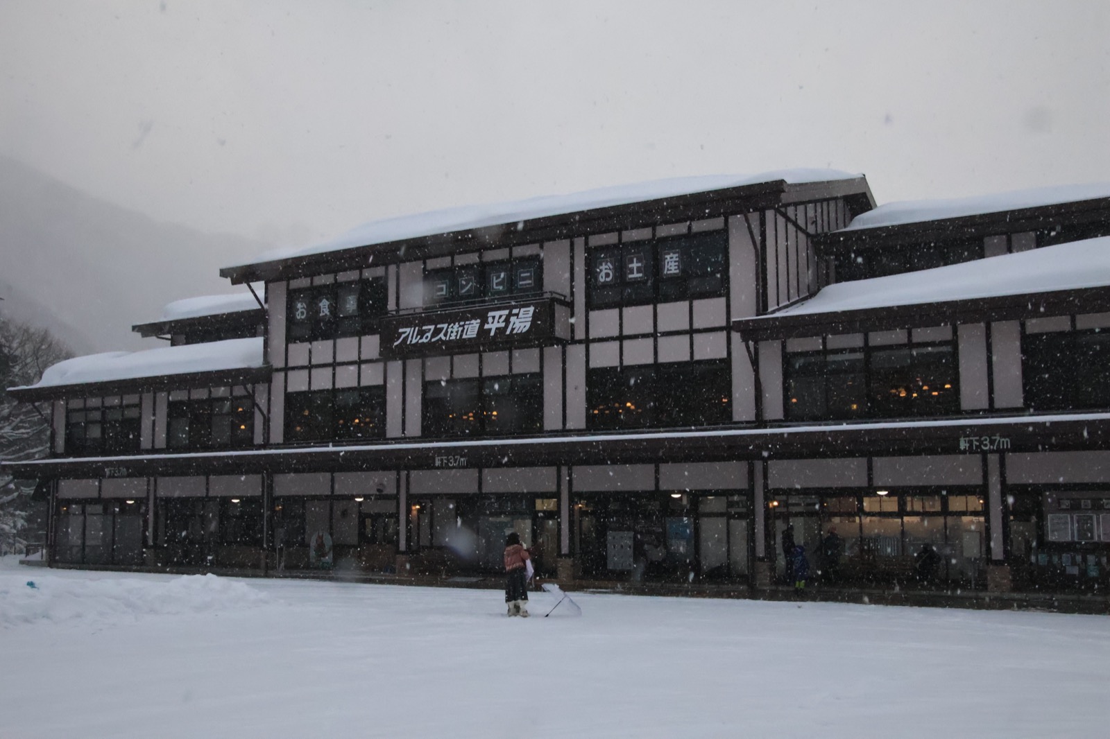 大雪中的平汤温泉街，一栋写着「アルプス街道 平湯」的传统建筑屋顶覆满积雪