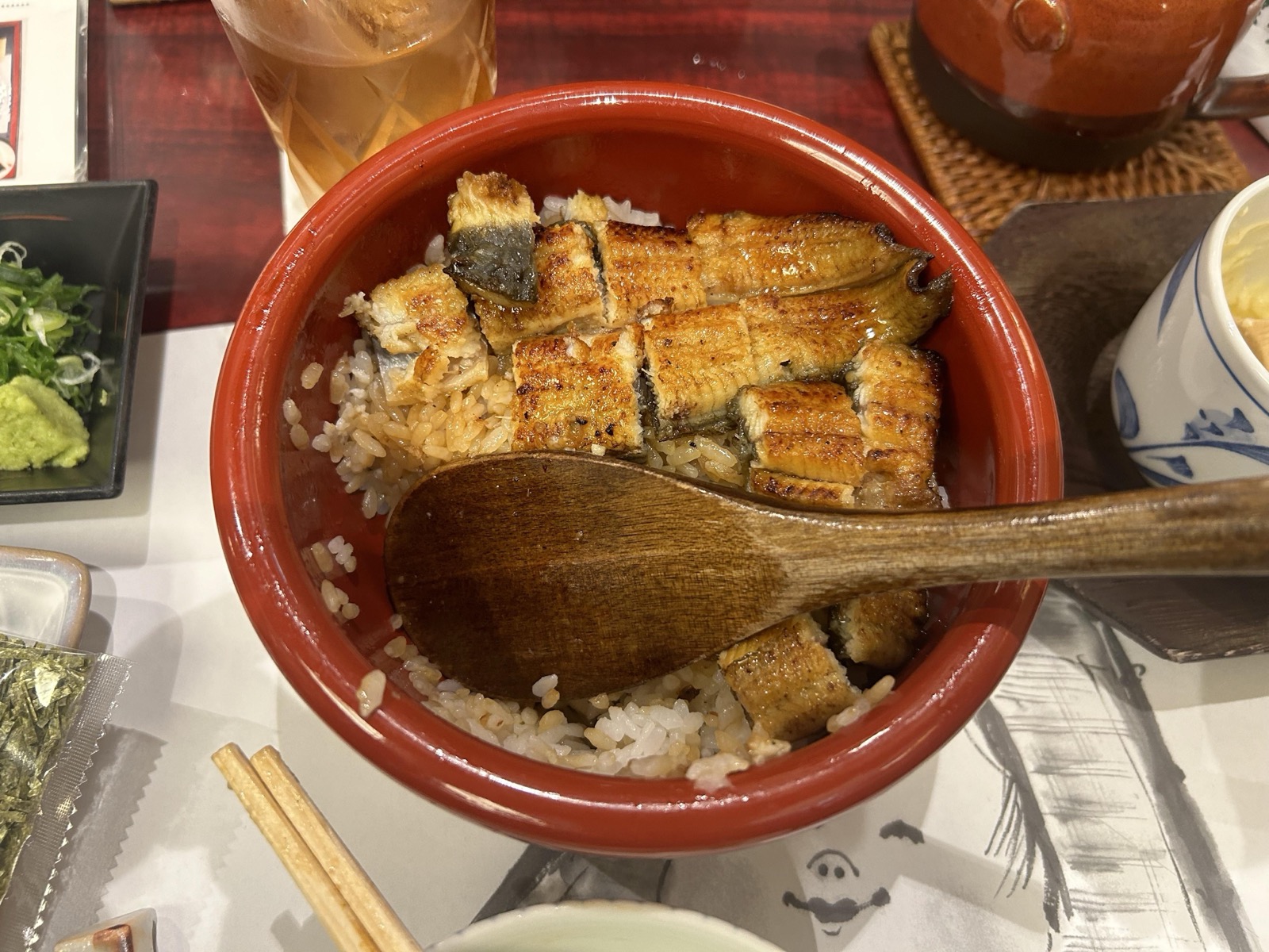 一只红色木碗盛着名古屋鳗鱼饭，烤得焦香的鳗鱼铺在米饭上，配着葱花与山葵
