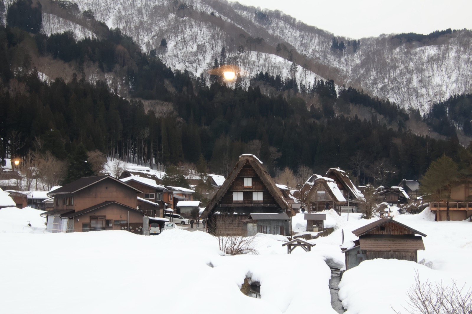 雪山脚下成片的合掌屋村落，屋顶与田野都被白雪覆盖