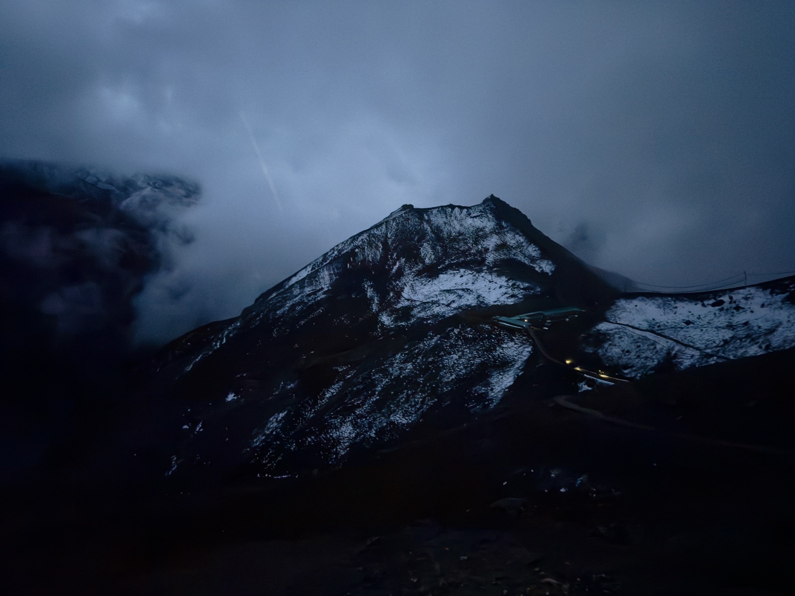 黎明前幽蓝的天色下，覆雪的山脊轮廓与山间几点高营地灯火