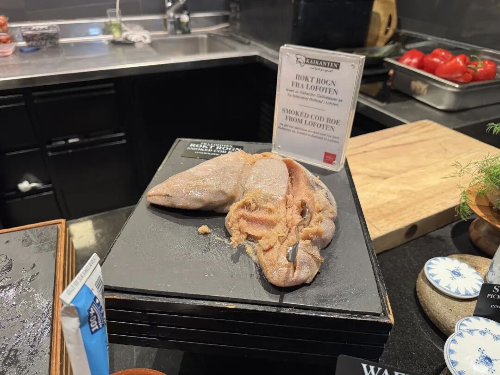 黑色石板上摆着来自罗弗敦的烟熏鳕鱼籽，配有英文标签 SMOKED COD ROE FROM LOFOTEN，旁边是樱桃番茄与切菜木板