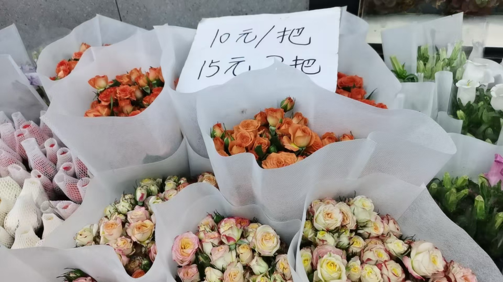 斗南花市里成束包好的玫瑰，橙色、粉色、香槟色层层叠叠，中间立着一张「10 元/把」的手写价签